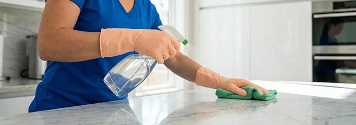 Maid service worker spraying and wiping a kitchen countertop with a microfiber cloth for sanitizing, Wichita, KS.
